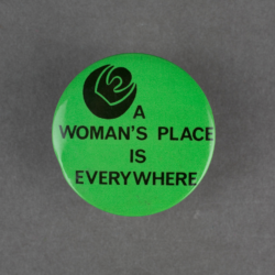 A lime green badge with black text that says a womans place is everywhere. There is also a silhouette of a rose printed in black.