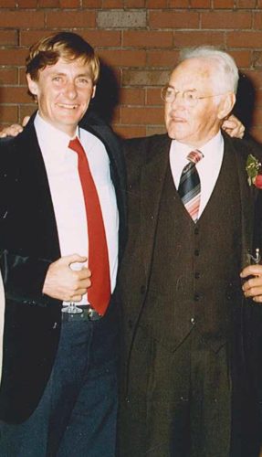 John Bannon standing with Clyde Cameron at his 70th birthday party. John is wearing a blue suit with a red tire and CLyde is wearing a brown suit and a white shirt.