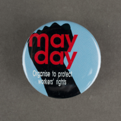 A blue badge with a black fish on it with the text May Day overlayed in red.