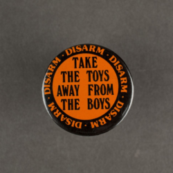 An orange badge with black text that says take the toys away from the boys.