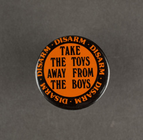 An orange badge with black text that says take the toys away from the boys.