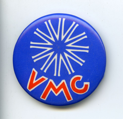 A bright blue badge with a white twelve pronged star on the top half and capital red letters on the bottom half spelling V M C.