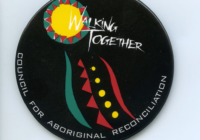 A black badge with white text saying Walking Together. There are some aboriginal designs on the badge in yellow, ochre red and eggshell green.