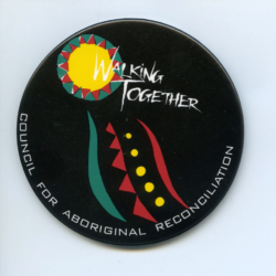 A black badge with white text saying Walking Together. There are some aboriginal designs on the badge in yellow, ochre red and eggshell green.