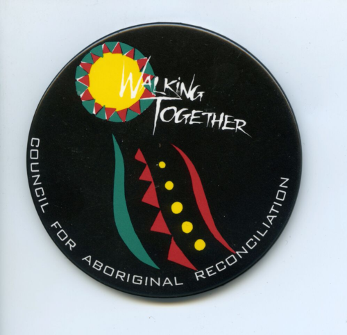 A black badge with white text saying Walking Together. There are some aboriginal designs on the badge in yellow, ochre red and eggshell green.