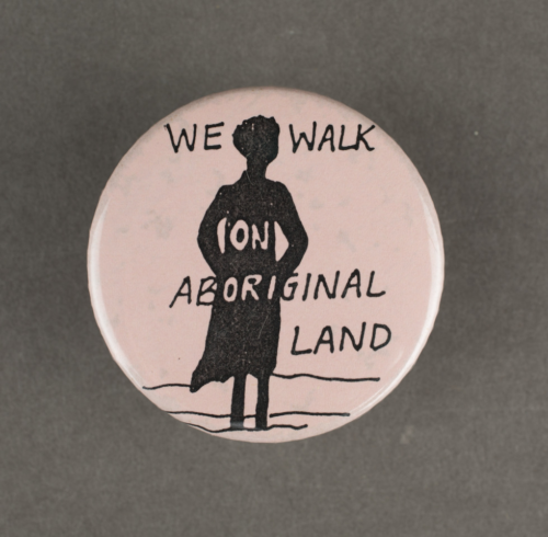 A light pink badge with the silhouette of a woman and the words we walk on aboriginal land over laid.