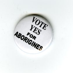 A white badge with black text that reads Vote Yes for Aborigines.