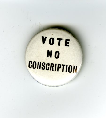 A white badge with black writing. The words read Vote No Conscription.
