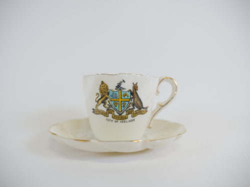 A small white teacup and saucer with the coat of arms for Adelaide City Council on the front.