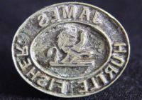 A small metal sealing stamp with the name James hurtle fisher embossed into it. In the centre is a small depiction of a lion.