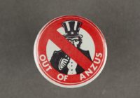 a badge with America's uncle sam in the middle of re circle with a cross through it. Also on the badge is the slogan 'out of ANZUS'