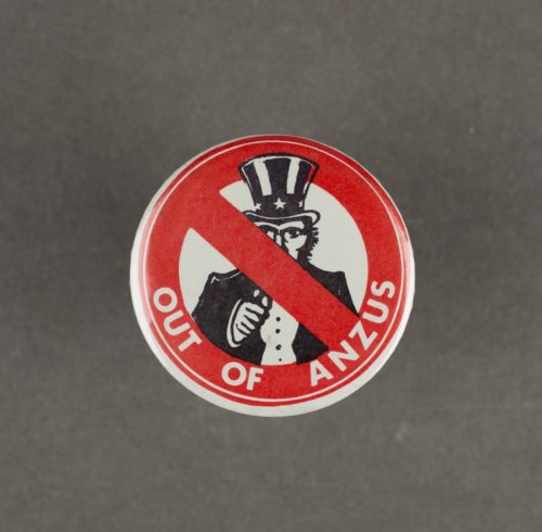 a badge with America's uncle sam in the middle of re circle with a cross through it. Also on the badge is the slogan 'out of ANZUS'