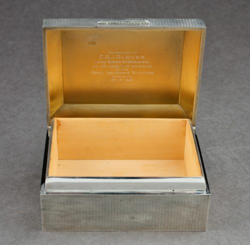 A small silver box with an open lid. The inside of the box is made from wood.