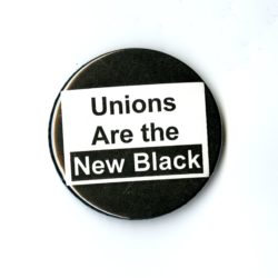 A black badge with a white square in the center. In the square is the phrase Unions are the New Black.