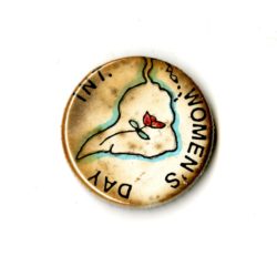 A small discolored white badge whihc the words INT. Women's Day written on it in black text. In the Centre if an outline of South America with a rose inside of it.